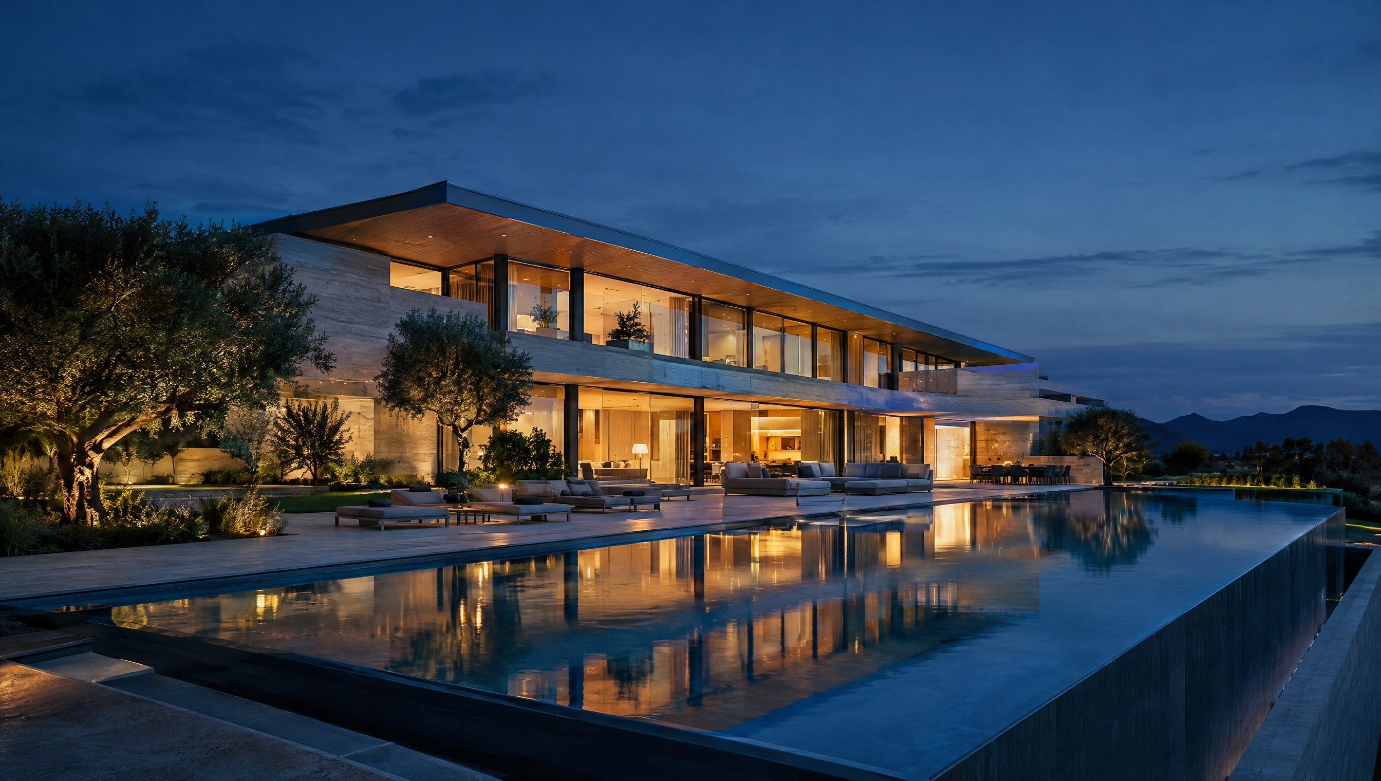 Contemporary travertine mansion at dusk with an infinity pool reflecting warm interior lights